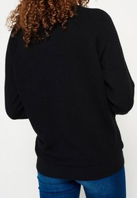 Felpa nera con scollatura arrotondata e maniche lunghe. Presenta polsini e orlo a coste, oltre a un tessuto morbido e testurizzato.