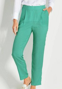 Grün gemusterte Hose mit geometrischem Design, geradem Bein, Eingrifftaschen und weichem Stoff. Kombiniert mit einem weißen Hemd und leichter Schuhmode.