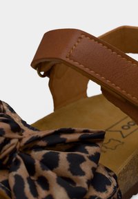 Sandale en cuir marron avec un nœud en tissu imprimé léopard sur l'avant et une semelle en liège.
