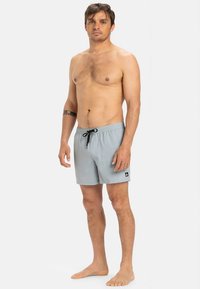 Sivé plavkové šortky so sťahovacou šnúrkou, bočnými vreckami a čiernou nášivkou s logom na leme. Ľahká tkanina a voľný strih.