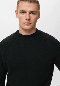Maglione nero a maglia con scollo rotondo, maniche raglan e una texture morbida. Design semplice senza motivi o dettagli in metallo.