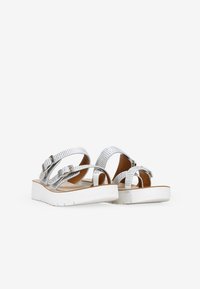 Sandalias plateadas con tiras entrelazadas, detalles texturizados, suela de plataforma baja y hebillas ajustables en una plantilla de color marrón claro.