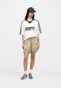 Fehér és fekete galléros mez "ESPN" grafikával, khaki rövidnadrággal és szürke futballcipővel párosítva. Fekete sapka logóval.