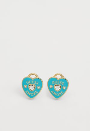 Gold-tone heart-shaped earrings with turquoise enamel, featuring “GUESS AMORE” text and clear crystal accents in the center and sides.