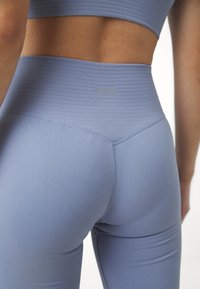 Lichtblauwe naadloze leggings met een geribbelde hoge taille en een soepele textuur. Bevat een klein merkembleem op het achterste taillegebied.