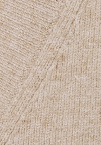 Beige kötött textília bordázott felülettel. Átlós vonalakat és finom variációkat mutat a szövés mintázatában, így lágy megjelenést kölcsönöz.
