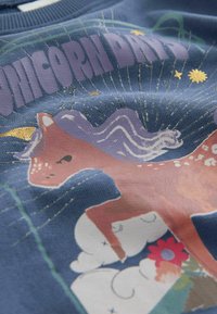 Niebieska tkanina z fantazyjnym wzorem jednorożca w odcieniach różu i fioletu, z białymi chmurami i kolorowymi kwiatami, wzbogacona złotymi akcentami.