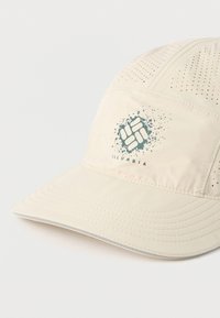 Ανοιχτό μπεζ καπέλο με διάτρητο ύφασμα, με κεντρικό λογότυπο σε σκούρο τιρκουάζ και δομημένο γείσο. Ορατές ραφές στις επιφάνειες.