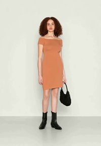 Vestido justo em tom ferrugem, com decote ombro a ombro e comprimento até ao joelho, de textura suave, combinado com uma mala de mão tecida preta e botins.