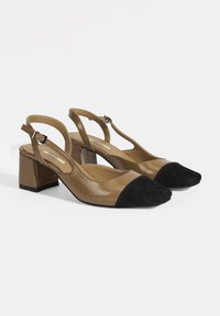 Tan leather slingback shoes with a black suede cap toe, block heels, and a thin ankle strap. Smooth texture with a classic design.