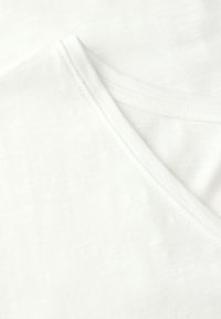 Hvid bomulds T-shirt med V-hals design, glat tekstur og subtilt vævet mønster. Kanten har en pæn syfinish.