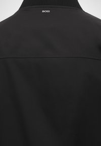 Vue arrière d’une veste noire avec col côtelé et petit logo blanc « "BOSS" » centré sous le col.