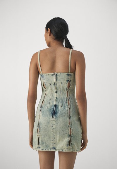 Denimkjole i lys blå med justerbare stropper, en tettsittende design og utskjæringer langs sidene og glidelås bak.