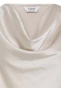 Col de blouse en satin couleur crème avec encolure drapée style bénitier et étiquette "b.young The Collection" visible au col.