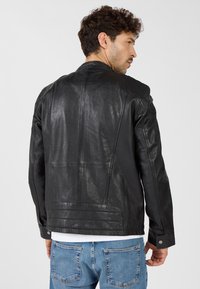 Schwarze Lederjacke mit glatter Textur, ausgestattet mit gesteppten Schulterakzenten und taillierter Passform, kombiniert mit blauen Jeans.