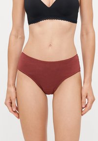 Burgunderfarbene Baumwollslips mit glattem Material, mittelhohem Schnitt und gewellten Kanten, kombiniert mit einem schwarzen, kabellosen Bralette darüber.