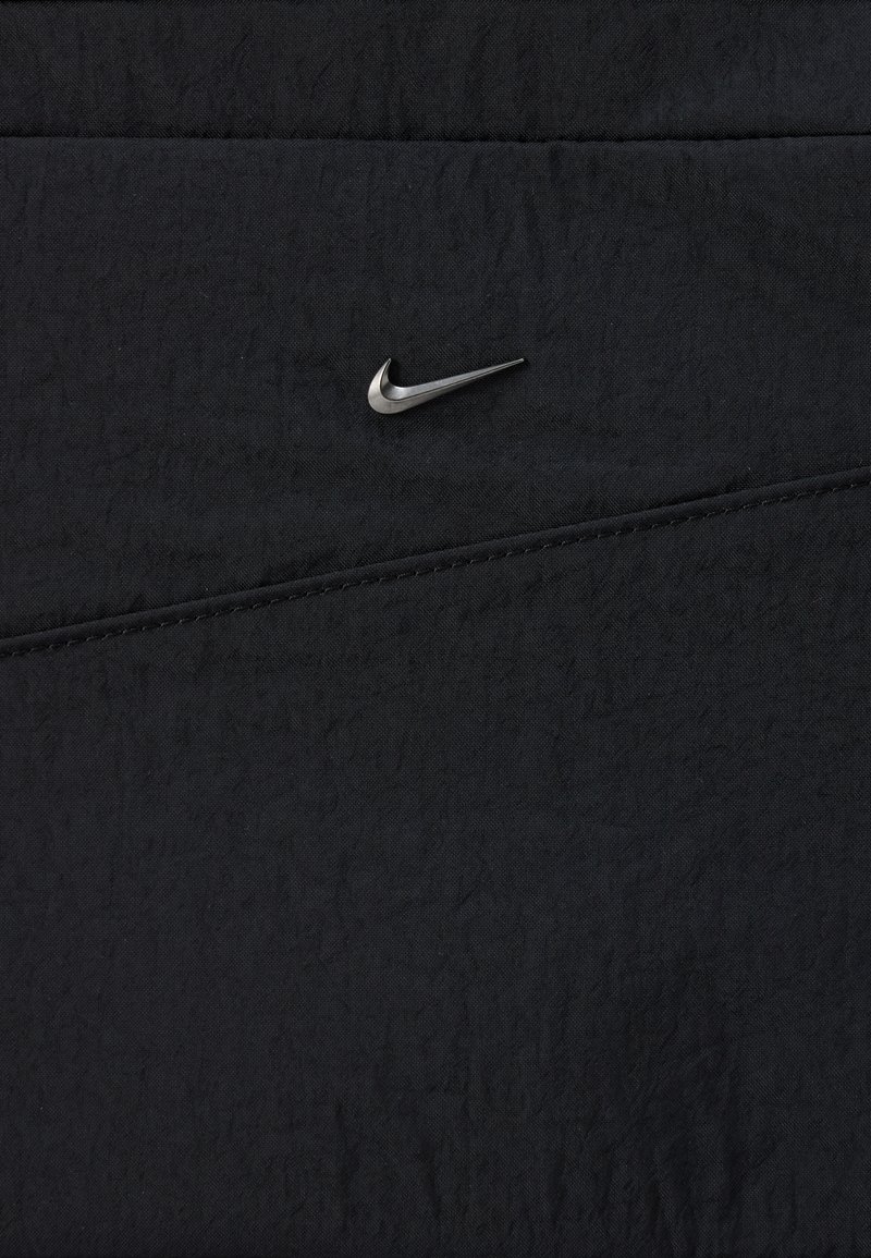 Tela negra con una costura diagonal cosida y un pequeño logotipo plateado de Nike Swoosh centrado cerca de la parte superior.