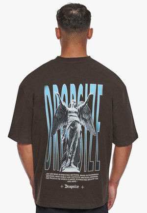 Brown oversized T-shirt featuring a graphic print of a statue with wings, blue text, and intricate detailing on the back.