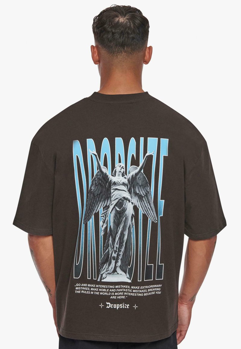 Brun oversized T-skjorte med grafisk trykk av en statue med vinger, blå tekst og intrikate detaljer på baksiden.