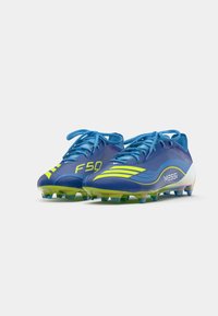 Blue football cleats with yellow accents, featuring a textured surface, laces, and molded studs. Displays "F50" and "MESSI" branding.