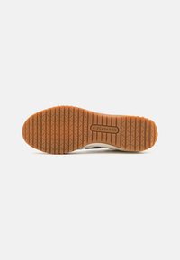 Rubber shoe sole with a textured grip pattern, featuring a light brown color. The sole has a logo embossed in the center.