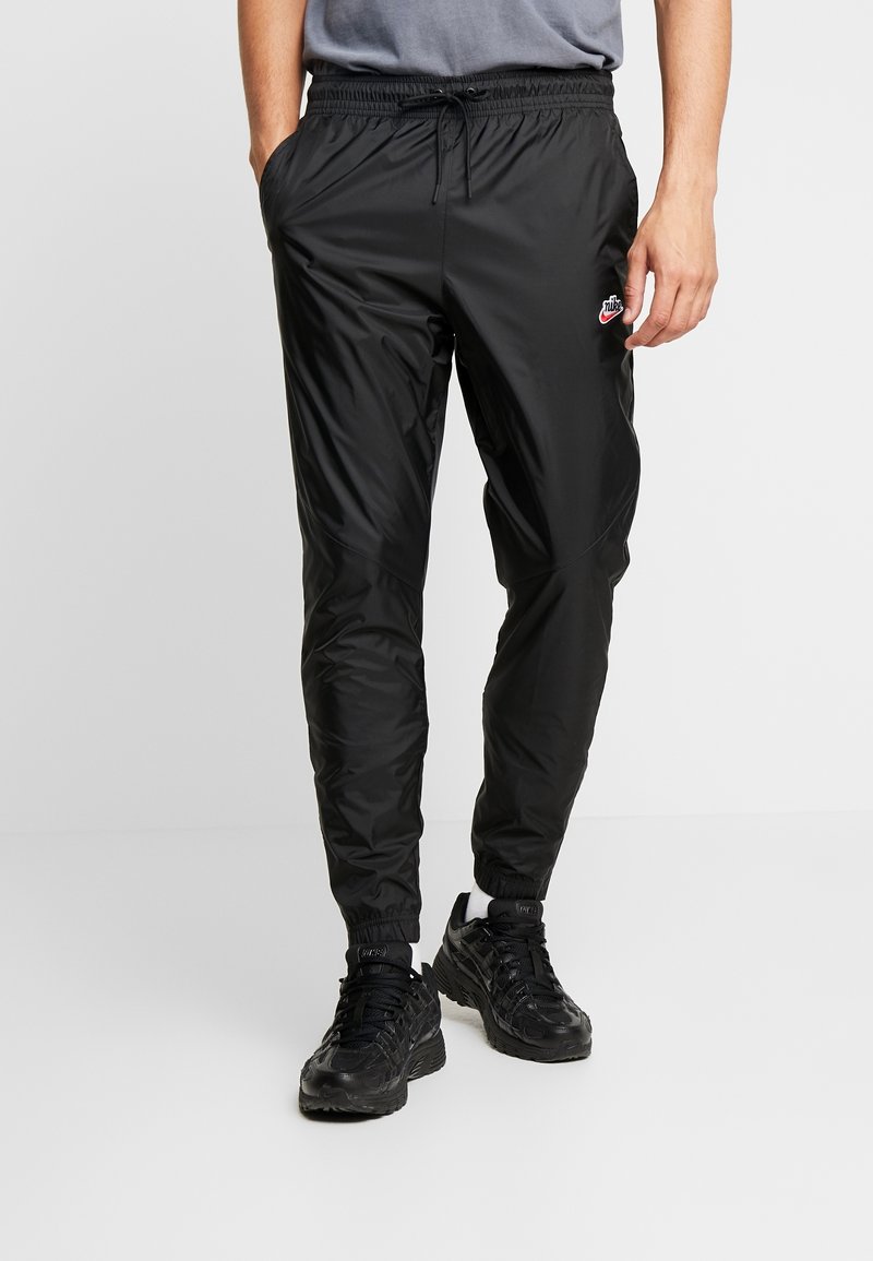 Mustat urheiluhousut, jotka on valmistettu kevyestä, kiiltävästä materiaalista. Niissä on joustava vyötärönauha, jossa on kiristysnyöri, ja nilkkakiinnitykset. Pieni logodetaili.