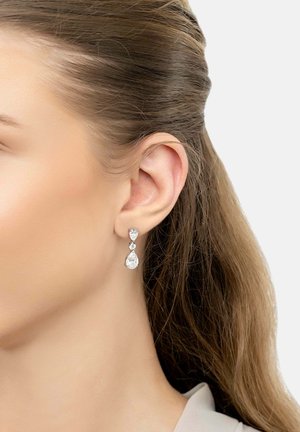 Drop earrings featuring clear gemstones in pear and round shapes, set in a silver-tone metal, hanging below the earlobe.