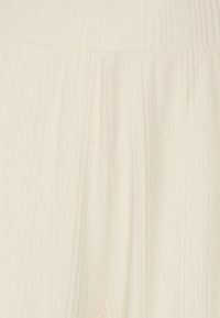 Geplooide stof, zachte off-white kleur, met verticale ribbels en een vloeiende uitstraling. Lichtgewicht materiaal met een gladde textuur.