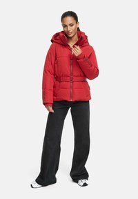 Red padded jacket with a hood, front zipper, and belt. Worn with black wide-leg pants and white sneakers. Smooth texture with quilted pattern.