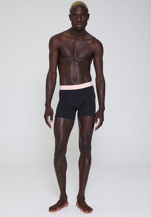 Sorte bokser-shorts med en lyserød elastisk talje. Fremstillet af strækbart stof, der sidder tæt til kroppen, med en glat tekstur.