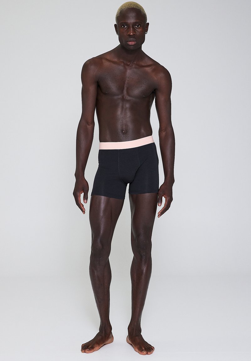 Sorte bokser-shorts med en lyserød elastisk talje. Fremstillet af strækbart stof, der sidder tæt til kroppen, med en glat tekstur.