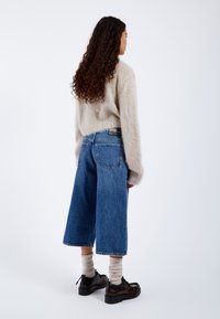 Beżowy puszysty sweter, luźne niebieskie jeansy w kroju cropped, kremowe skarpetki do kolan i czarne sznurowane buty. Gładka tekstura i swobodny krój.