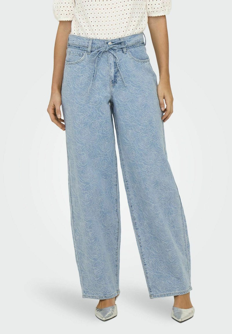 Pantalon en denim bleu clair à jambes larges avec un motif de roses et une ceinture à nouer. Le tissu présente une texture subtile, avec des poches avant et une taille haute.