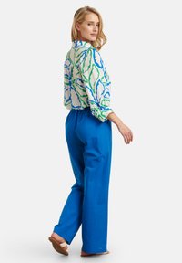 Colorful blouse with green and blue floral pattern, collared neckline, and loose long sleeves paired with bright blue trousers.