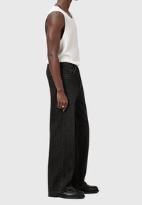 Jean noir à jambes larges en denim, associé à un débardeur blanc côtelé. Détails remarquables : une taille haute et des coutures minimales sur les poches.