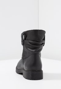 Czarny skórzany botek za kostkę z lekko luźną cholewką, zaokrąglonym noskiem i teksturowaną podeszwą. Model posiada boczny pasek i minimalistyczne przeszycia.