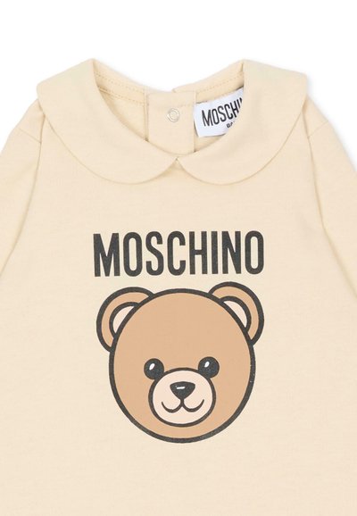 Cremefarbener Stoffoberteil mit Kragen und einem braunen Bär-Grafikdruck mit schwarzer Umrandung sowie dem Schriftzug "MOSCHINO" oben.