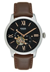 Montre Fossil automatique avec un cadran noir, des index heures en or rose, et un boîtier transparent dévoilant les rouages. Bracelet en cuir marron avec couture.