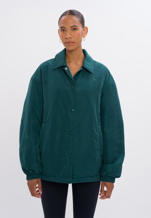 Türkisfarbene, oversized Jacke aus glattem Material mit einem Kragen, vorderen Druckknöpfen, elastischen Bündchen und einem dezenten Logo auf der Brust.