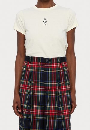Persoon draagt een wit shirt met korte mouwen met een ankerlogo en een rood, blauw en groen geruite geplooide rok.