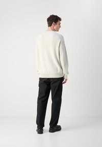 Maglione grigio chiaro a coste con maniche lunghe, abbinato a pantaloni cargo neri. L'outfit presenta una vestibilità comoda e un tessuto testurizzato.