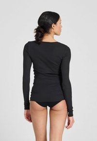 Fekete, hosszú ujjú felső bordázott textúrával, testhez álló fazonnal, kerek nyakkivágással és sima felülettel. Fekete bikini alsóval párosítva.