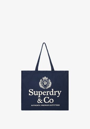 Granatowa torba typu tote z długimi uchwytami, z białym napisem ""Superdry & Co Authentic Premium Outfitters"" i logo z wieńcem laurowym.