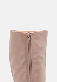 Stivale finto pelle rosa al ginocchio con zip frontale, texture liscia e bordo superiore arrotondato, caratterizzato da cuciture dettagliate lungo le cuciture.
