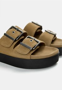 Bruine suède sandalen met twee brede banden, metalen gespen en een dikke zwarte plateauzool. Zachte textuur met zichtbare stiksels.