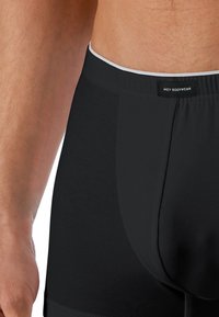 Boxer shorts neri da uomo realizzati in un tessuto morbido, con cintura elastica e una sottile bordatura bianca. Presentano un design aderente con una copertura confortevole.