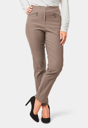 Tapered bruine broek gemaakt van rekbaar materiaal met twee voorzakken met rits en een gladde textuur, gecombineerd met zwarte hoge hakken.
