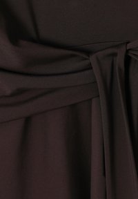 Tela de color marrón oscuro con una textura suave, que presenta un detalle de cintura anudada y pinzas, creando un diseño fluido. Los bordes están terminados de manera ordenada.