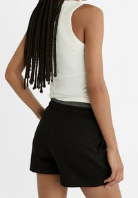 Černé bavlněné šortky s elastickým pasem, které jsou kombinovány s bílým žebrovaným tílkem. Zaměřeno na pohled zezadu a detaily textury látky.