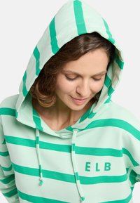 Világos zöld kapucnis pulóver széles zöld csíkokkal. Felszereltsége között szerepel a húzózsinór, elülső zseb és az "ELB" felirat, amely ugyanazzal a színnel készült.